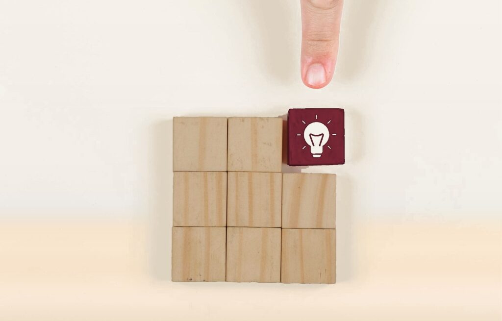 Cubes de bois et un cube bordeaux marqué d’une ampoule, désigné par un doigt